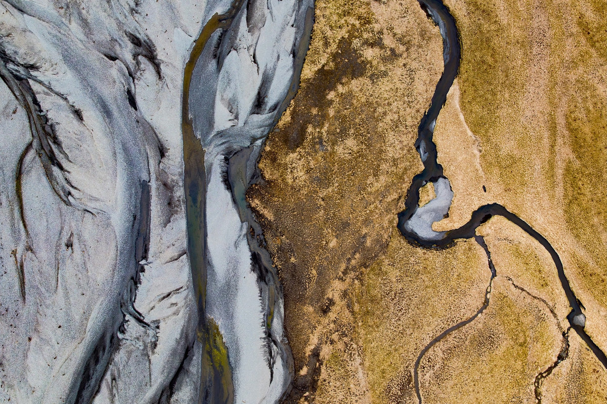 Gletscherfluss in Island von oben, grau-blaues Gletscherwasser trifft auf goldenes Flussdelta